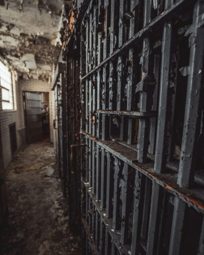 Eerie abandoned prison corridor with decaying rusty bars and peeling paint.
